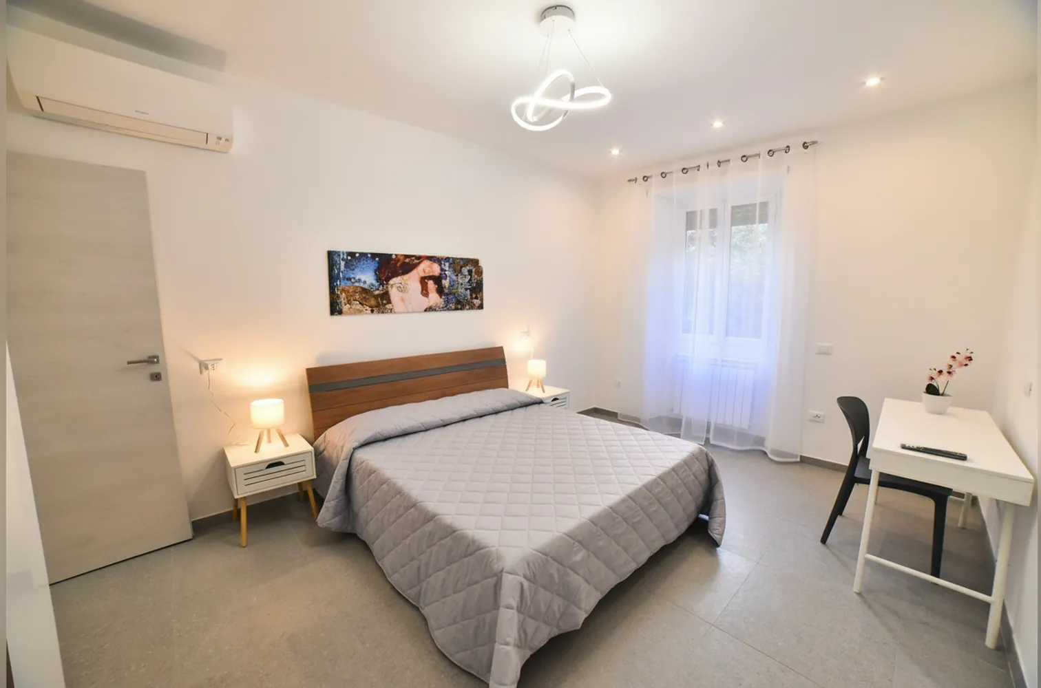 La camera matrimoniale con il letto in legno, i comodini, la scrivania bianca e la finestra con le tende